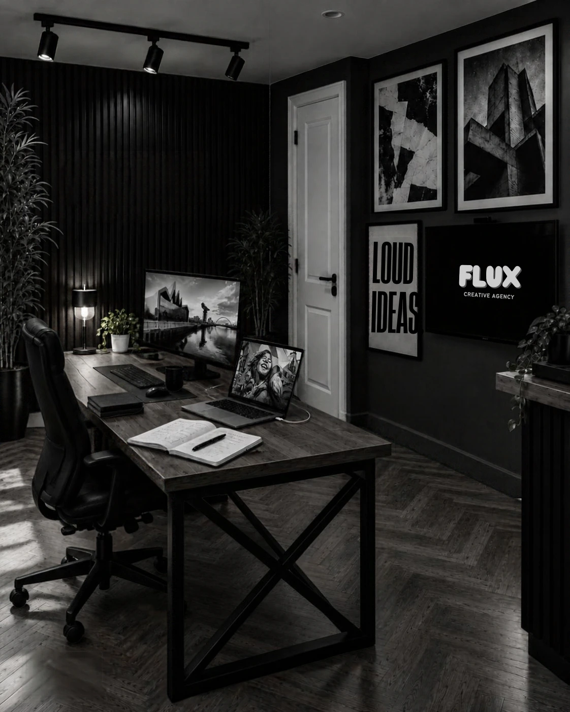 Black-and-white Flux workspace with a wooden desk, desktop and laptop screens, framed artwork and a Flux logo display